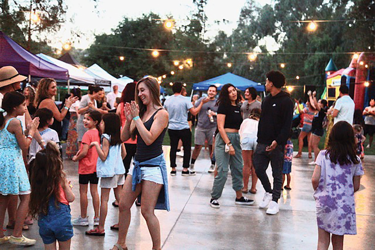 Group of people dancing outside of a festival with tents and a bouncy house around them.