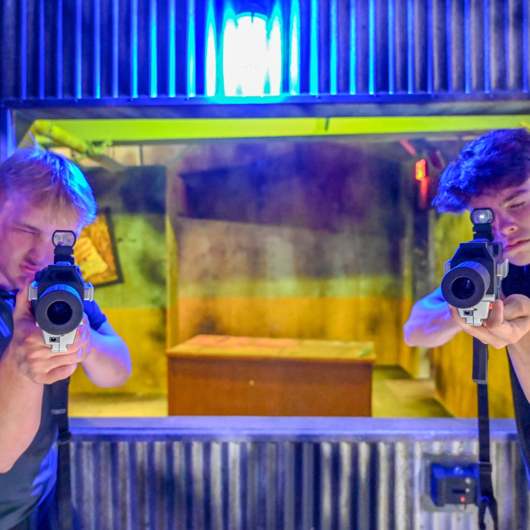 Two boys holding play guns in arcade area.