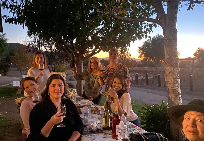 Group of women sitting outside at a table enjoying wine at a winery.