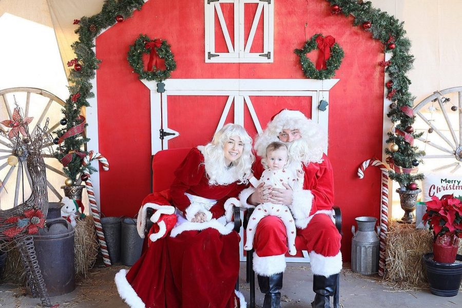 Santa and Mrs. Claus holding a baby in front of a red barn at Gilchrist Farm in Santa Clarita.